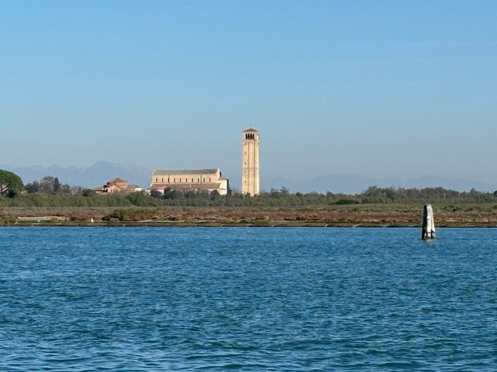 Panoramic view of the Basilica of Santa Maria Assunta and its bell tower on Torcello Island, surrounded by the Venetian Lagoon.