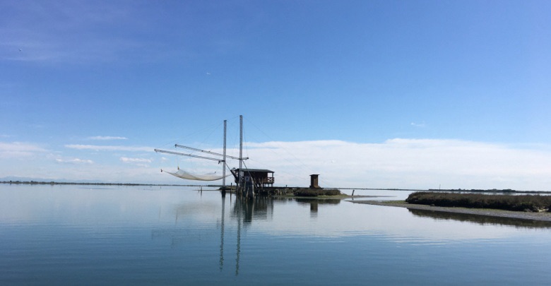 View of traditional fishing structures, called 'casoni', standing in calm waters with a clear blue sky in the background.