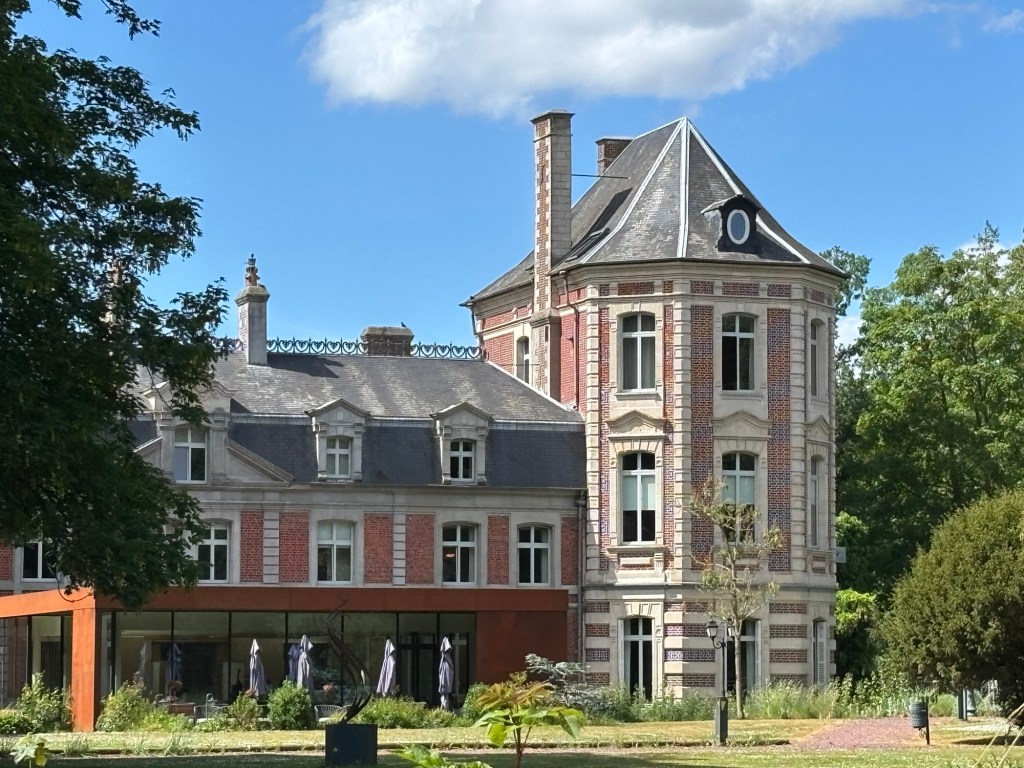 View of Chateau de Beaulieu showcasing a blend of historic and modern architecture surrounded by a lush garden and blue sky.