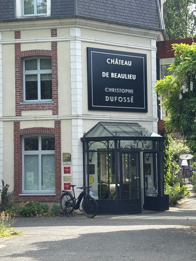Exterior view of Château de Beaulieu featuring a stylish entrance with a bicycle parked outside and signage displaying 'Château de Beaulieu' and 'Christophe Dufossé'.