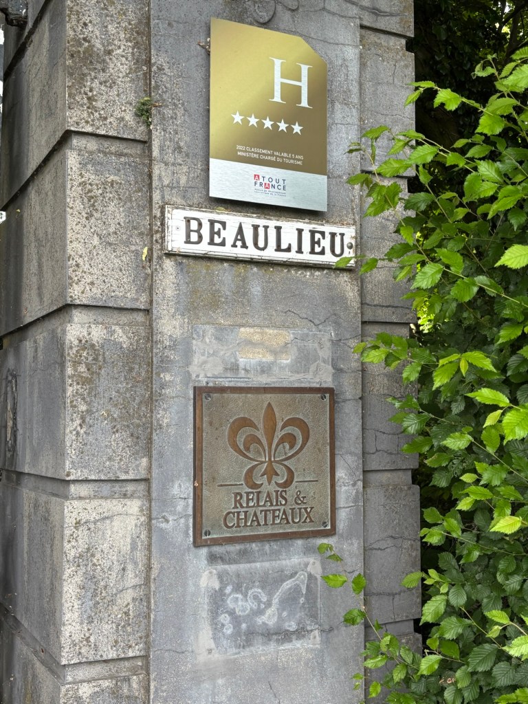 Sign indicating Chateau de Beaulieu, featuring a five-star rating and the Relais & Châteaux logo, surrounded by green foliage.
